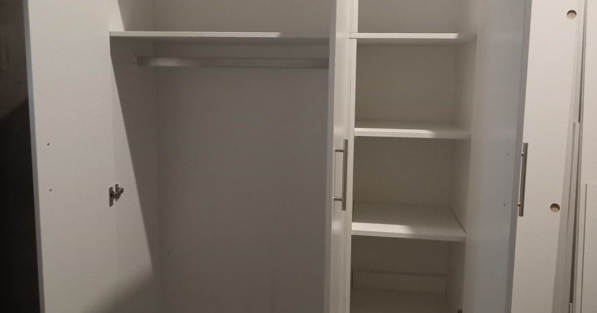 Open built-in bedroom cupboard showing shelves, drawers and hanging rail