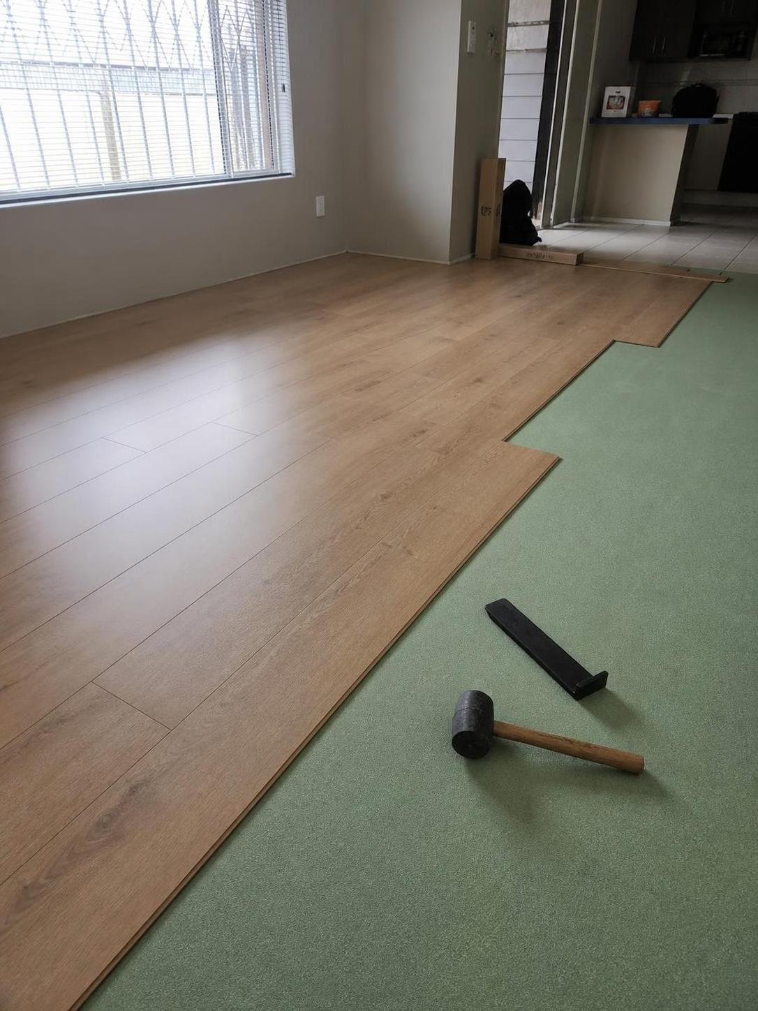 Light oak laminate flooring being installed over green underlay in a Cape Town lounge